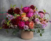 Vibrant spring floral arrangement in a peach vase featuring peonies, roses, and dahlias.