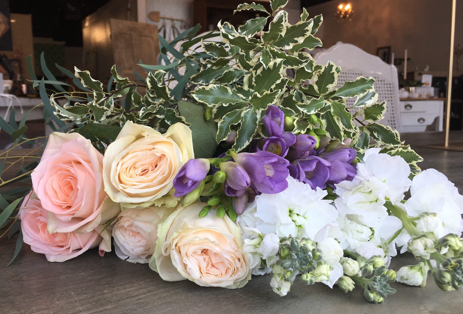 From left to right: Peach roses, cream Garden Roses, purple Freesia, white Stock. On top Feathered Eucalyptus and Variegated Pittosporum.