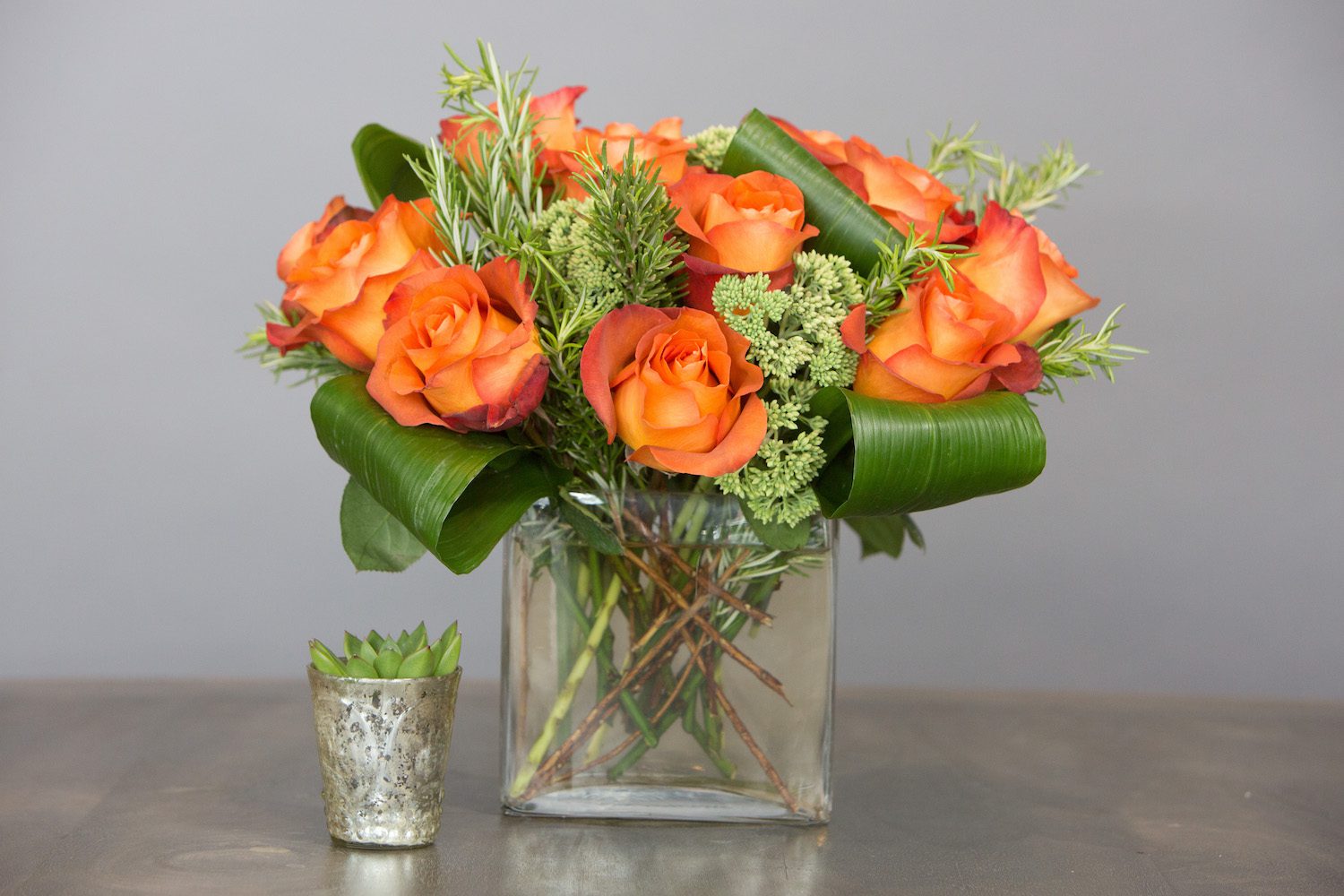 This "modern dozen" with burnt orange Roses is paired with a succulent in a small votive vase, sold separately.