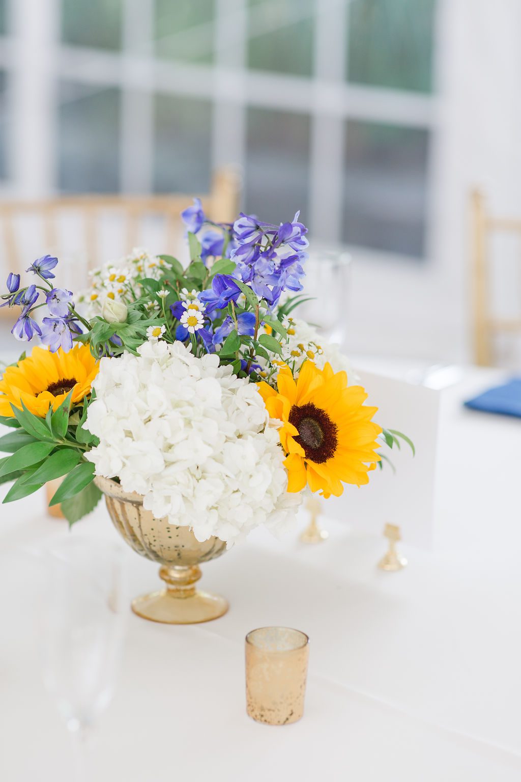 Centerpieces in an elegant gold compote with Sunflower and Delphinium for the blue in this couple’s palette. Photography by Emily Alyssa Photography.