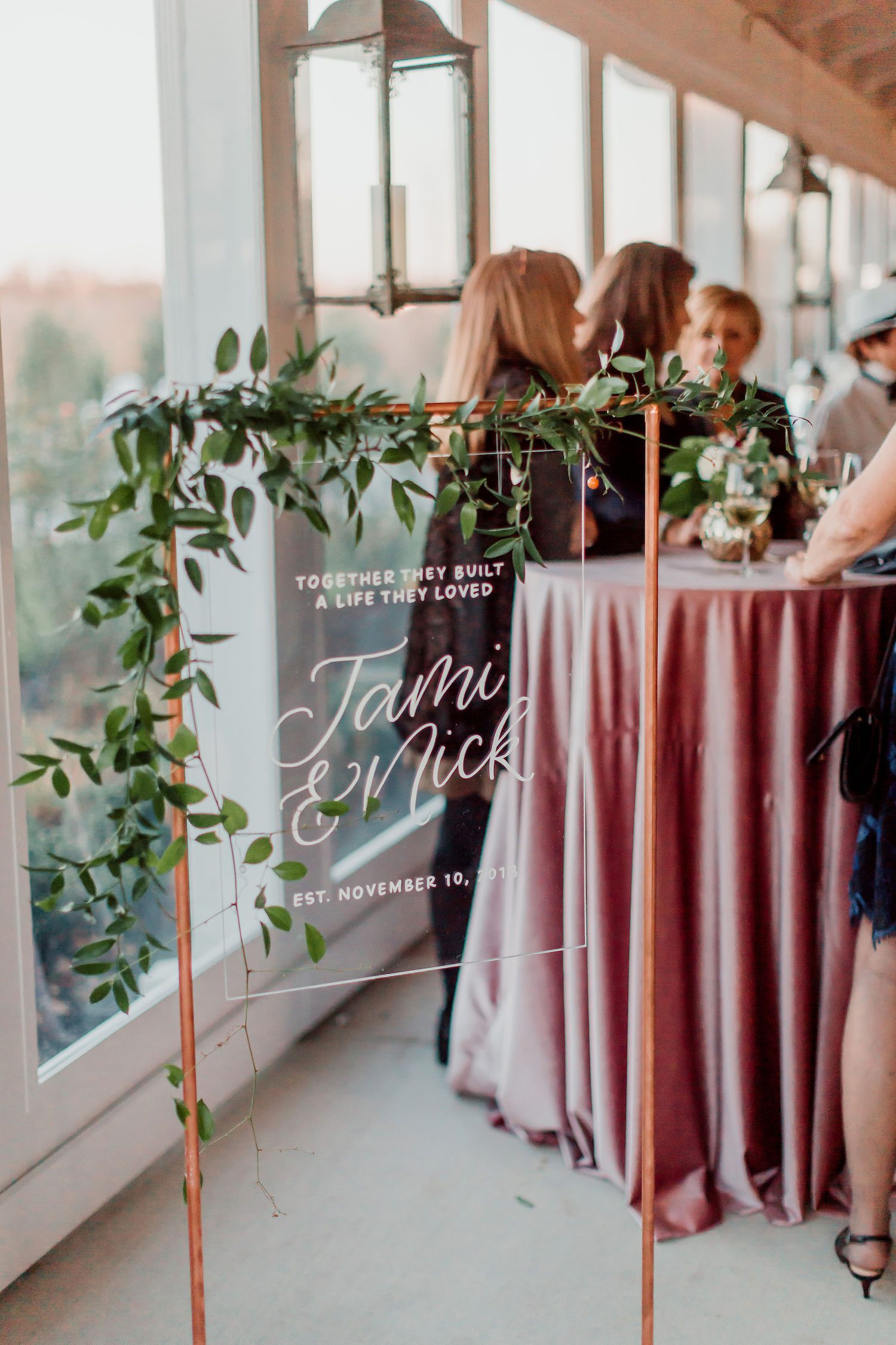 A copper and glass welcome sign with greenery at Shadow Creek. Photography by Hay Alexandra.