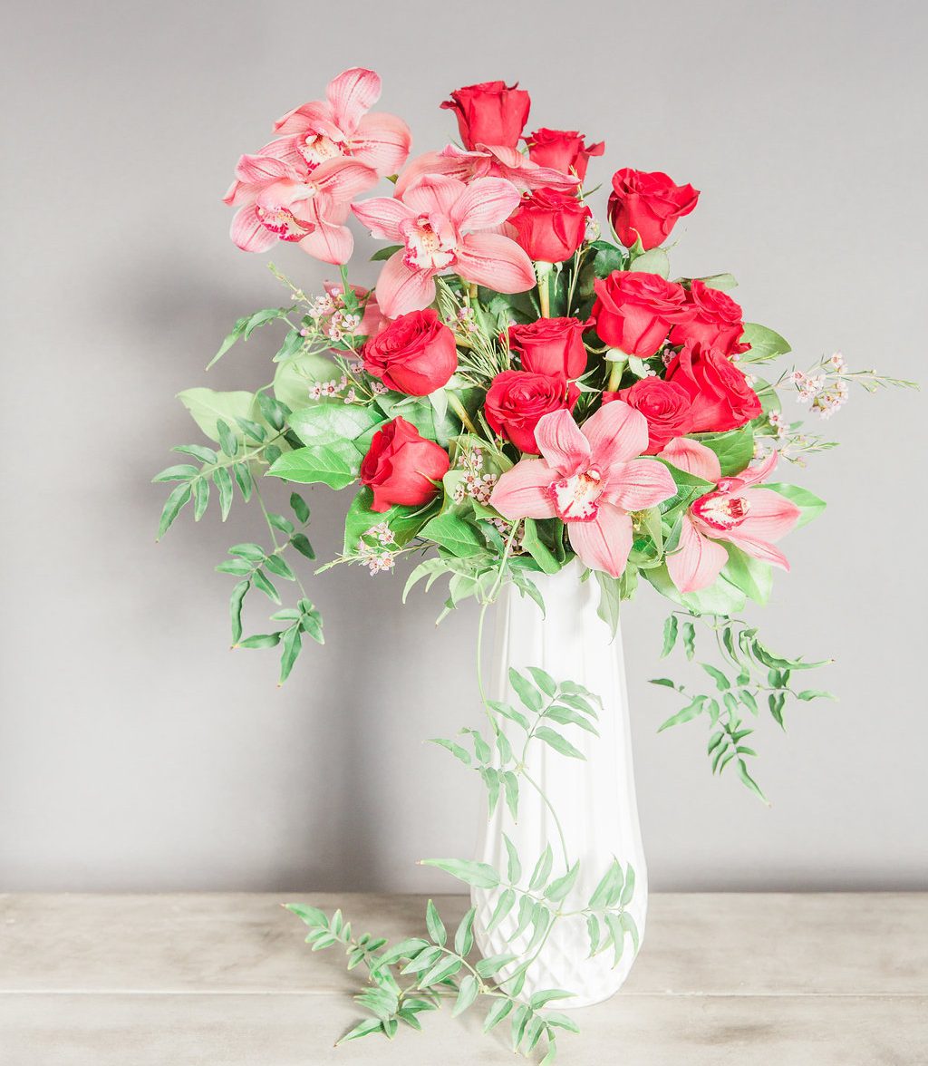 "Love You This Much" with Pink Cymbidium Orchids and Red Roses in an elegant white ceramic vase with a geometric pattern and gold lining.