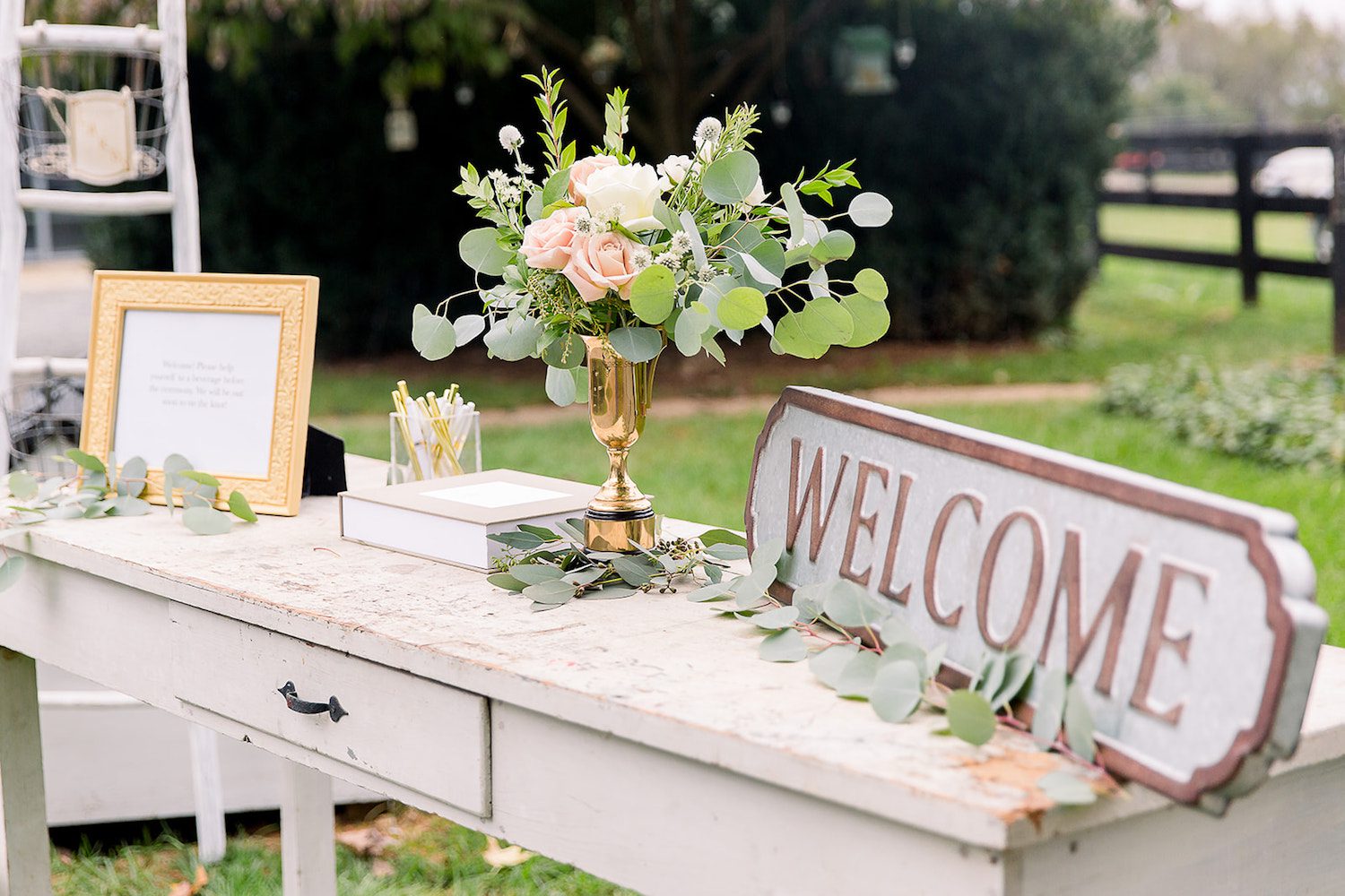 A welcome table honors loved ones who have passed or cannot attend with pink and white flowers, thistle and greenery. Photography by Nicole Adele.