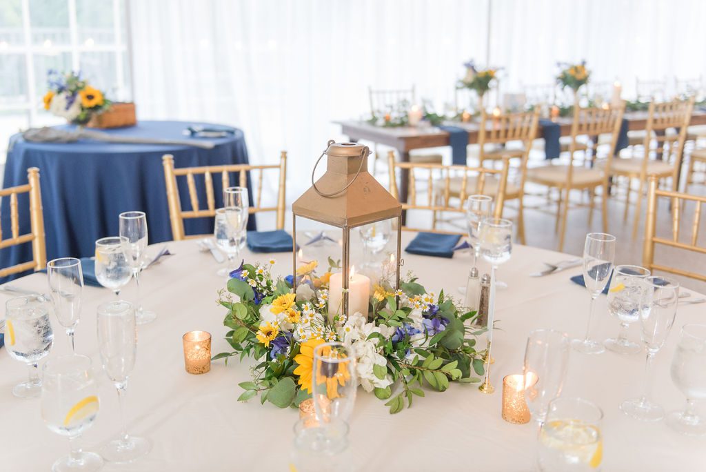 A second centerpiece option included Sunflowers and Delphinium in a wreath around this gold lantern. Photography by Emily Alyssa Photography at Rust Manor House.