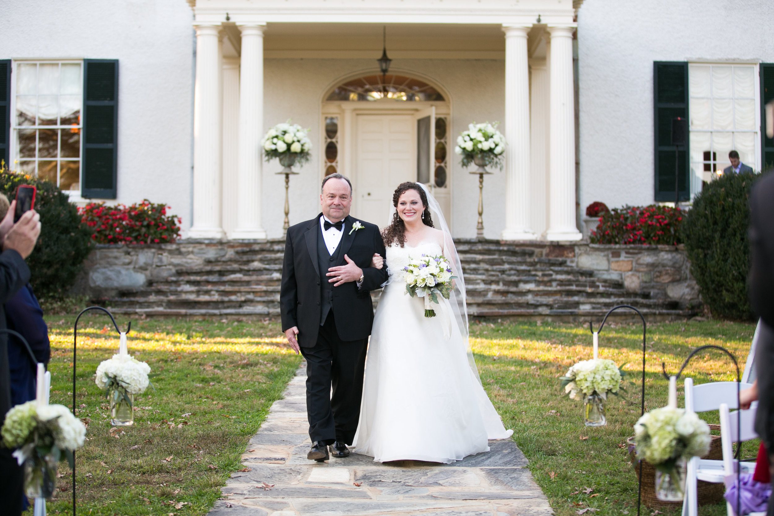 Duplicating the ceremony arrangements on the porch made all the different to enhance this lovely scene. We added simple vessels of white and green to bring color to the aisle.&nbsp;