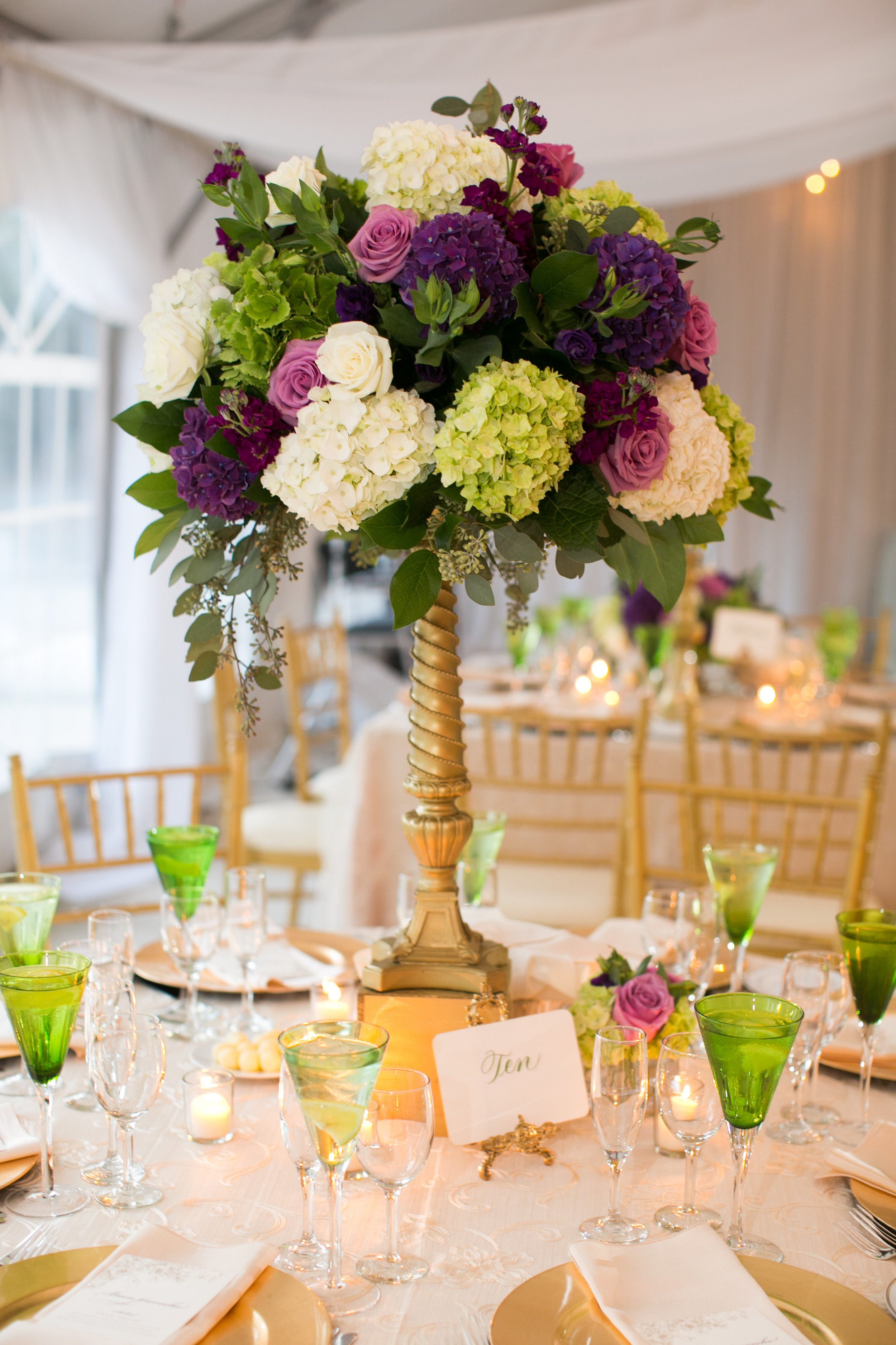 The tent was filled with two styles of table decor - this tall centerpiece in purple, white, lavender and green with an "old gold" vintage riser.&nbsp;
