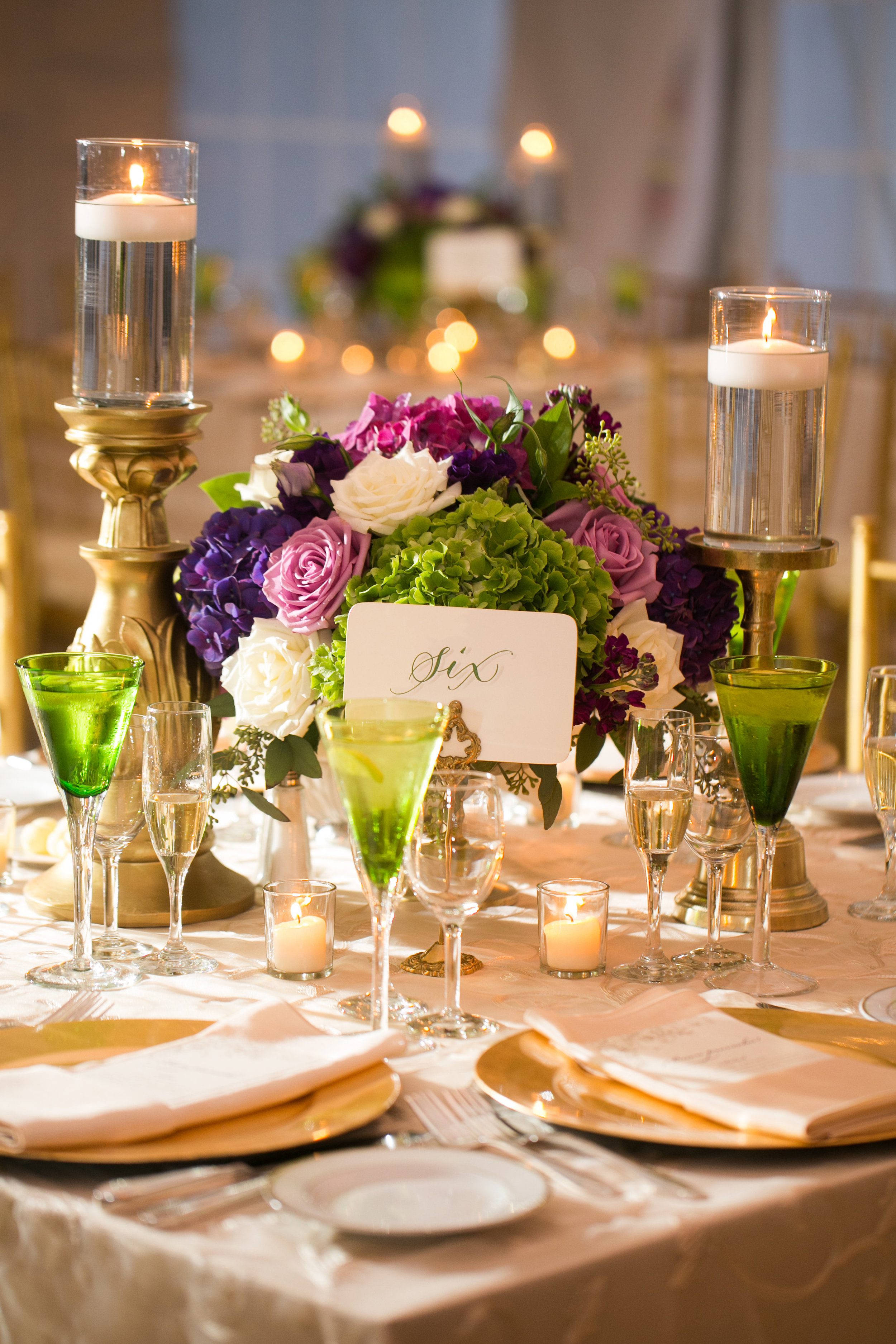 The low centerpiece in the tent was a lush purple, green, lavender and white arrangement in a gold pedestal vase, flanked by two timeless "old gold" candlesticks.&nbsp;